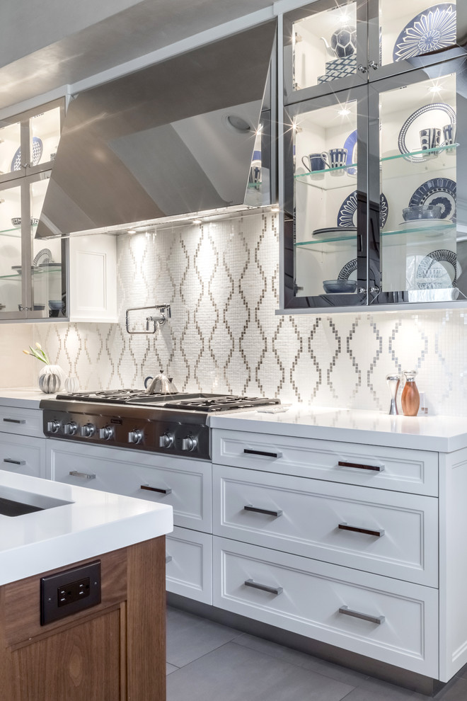 This is an example of a mid-sized transitional u-shaped eat-in kitchen in New York with an undermount sink, recessed-panel cabinets, white cabinets, solid surface benchtops, white splashback, stainless steel appliances, porcelain floors, with island and mosaic tile splashback.