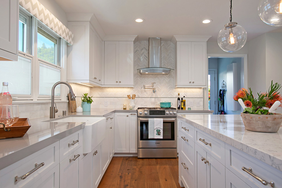 Transitional l-shaped kitchen in San Diego with a farmhouse sink, shaker cabinets, white cabinets, stainless steel appliances, medium hardwood floors, with island and brown floor.