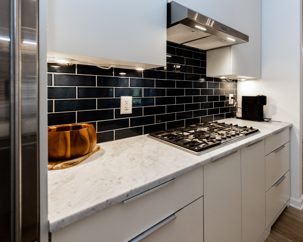 This is an example of a large scandinavian galley eat-in kitchen in Atlanta with an undermount sink, flat-panel cabinets, beige cabinets, marble benchtops, black splashback, subway tile splashback, stainless steel appliances, light hardwood floors, with island, brown floor and white benchtop.