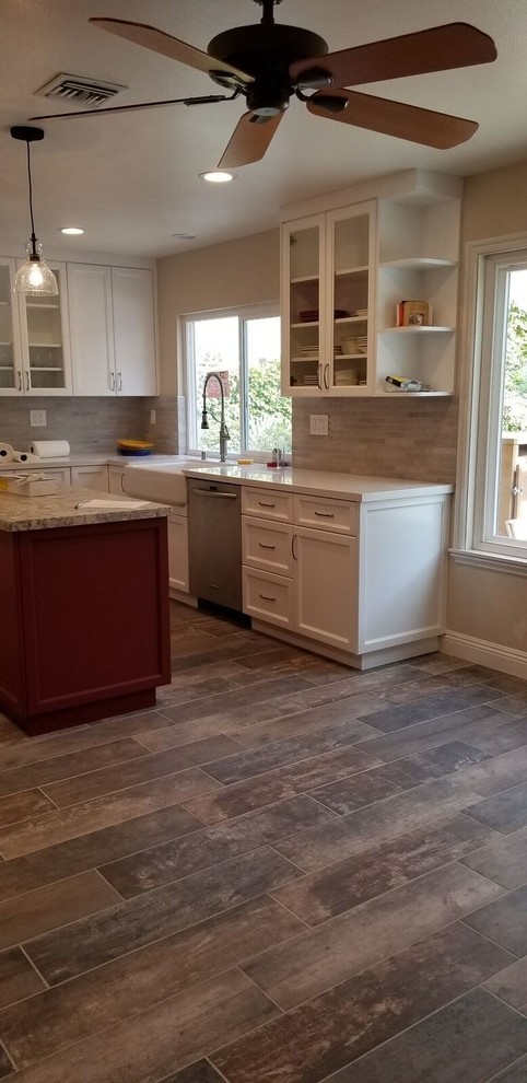 Large country u-shaped eat-in kitchen in Los Angeles with shaker cabinets, white cabinets, quartzite benchtops, beige splashback, stone tile splashback, stainless steel appliances, porcelain floors, with island, brown floor and white benchtop.