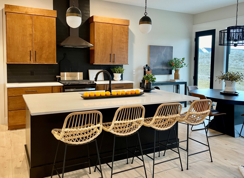 Design ideas for a large midcentury l-shaped open plan kitchen in Other with an undermount sink, flat-panel cabinets, medium wood cabinets, quartz benchtops, black splashback, subway tile splashback, black appliances, light hardwood floors, with island, brown floor and white benchtop.