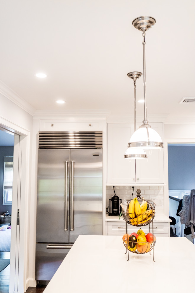 Enclosed kitchen - mid-sized transitional dark wood floor and brown floor enclosed kitchen idea in New York with a farmhouse sink, recessed-panel cabinets, white cabinets, quartzite countertops, white backsplash, subway tile backsplash, stainless steel appliances and an island
