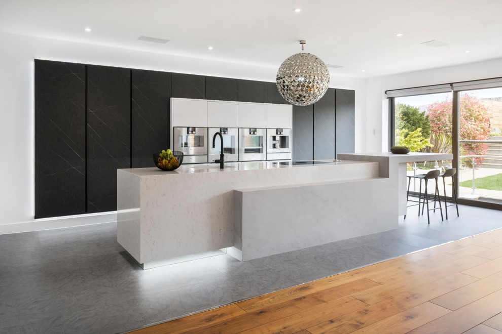 Foto på ett stort funkis grå kök med öppen planlösning, med grå skåp, bänkskiva i kvartsit, rostfria vitvaror, en köksö och grått golv