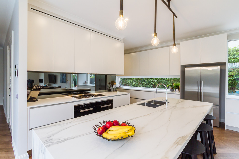 Inspiration for a large modern galley open plan kitchen in Melbourne with an undermount sink, flat-panel cabinets, white cabinets, marble benchtops, window splashback, stainless steel appliances, medium hardwood floors, with island, beige floor and white benchtop.