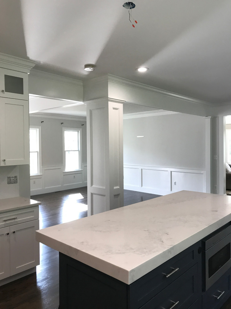 Photo of a large country u-shaped eat-in kitchen in Boston with a farmhouse sink, shaker cabinets, white cabinets, quartz benchtops, white splashback, ceramic splashback, stainless steel appliances, dark hardwood floors, with island, brown floor and white benchtop.