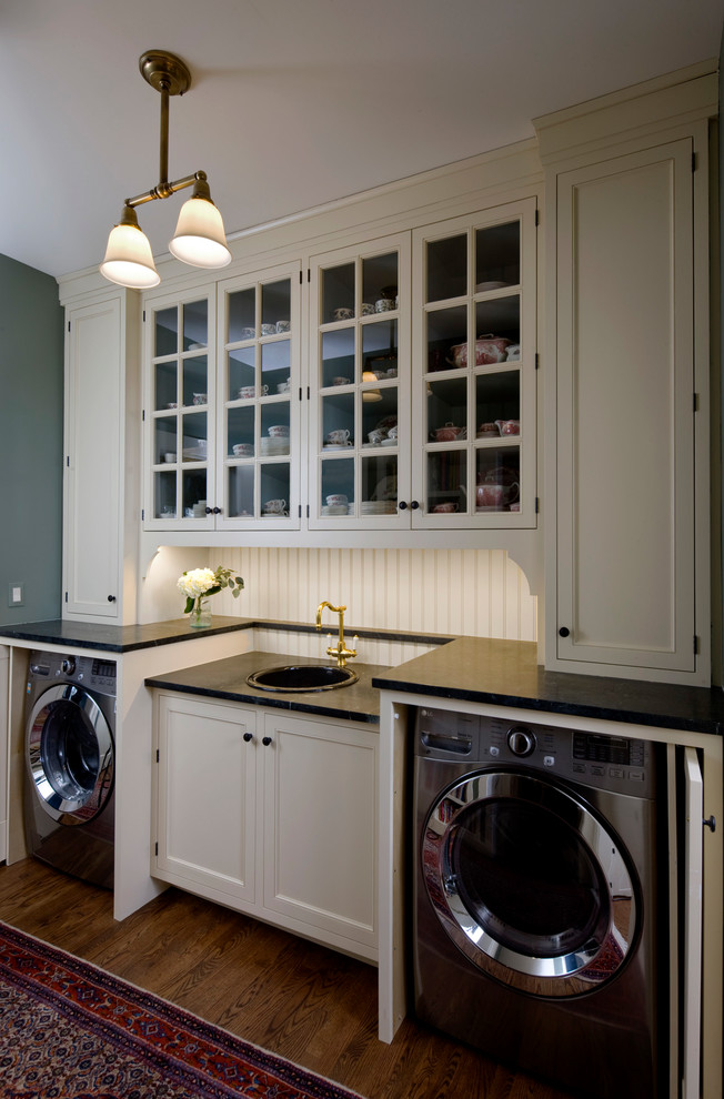 This is an example of a small traditional single-wall utility room in Chicago with a single-bowl sink, beaded inset cabinets, white cabinets, soapstone benchtops, green walls, medium hardwood floors, a concealed washer and dryer and black benchtop.