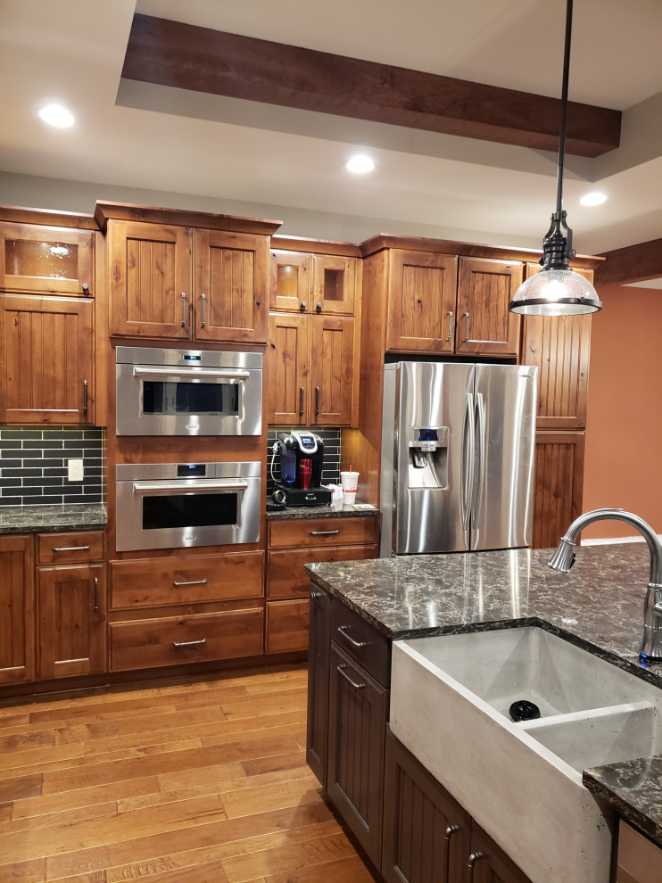 Kitchen - rustic medium tone wood floor kitchen idea in Grand Rapids with a farmhouse sink, recessed-panel cabinets, dark wood cabinets, quartz countertops, black backsplash, travertine backsplash, stainless steel appliances, an island and brown countertops