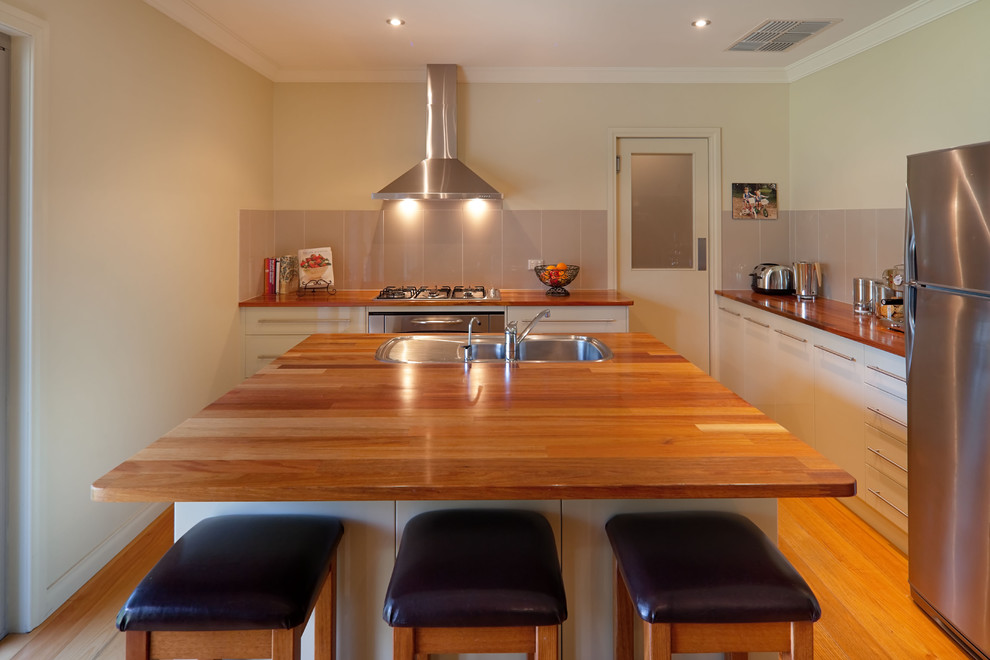 This is an example of a contemporary u-shaped separate kitchen in Sydney with a drop-in sink, flat-panel cabinets, white cabinets, wood benchtops, grey splashback, glass tile splashback and stainless steel appliances.