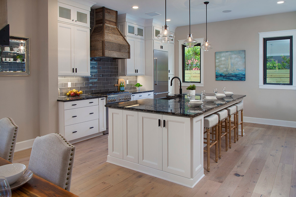 Example of a large transitional u-shaped light wood floor open concept kitchen design in Orlando with a farmhouse sink, shaker cabinets, white cabinets, quartzite countertops, gray backsplash, ceramic backsplash, stainless steel appliances and an island