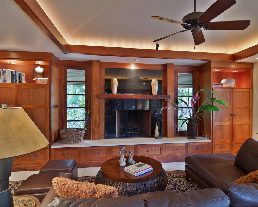 This is an example of a mid-sized tropical open concept family room in San Diego with beige walls, travertine floors, a standard fireplace, a stone fireplace surround and a concealed tv.