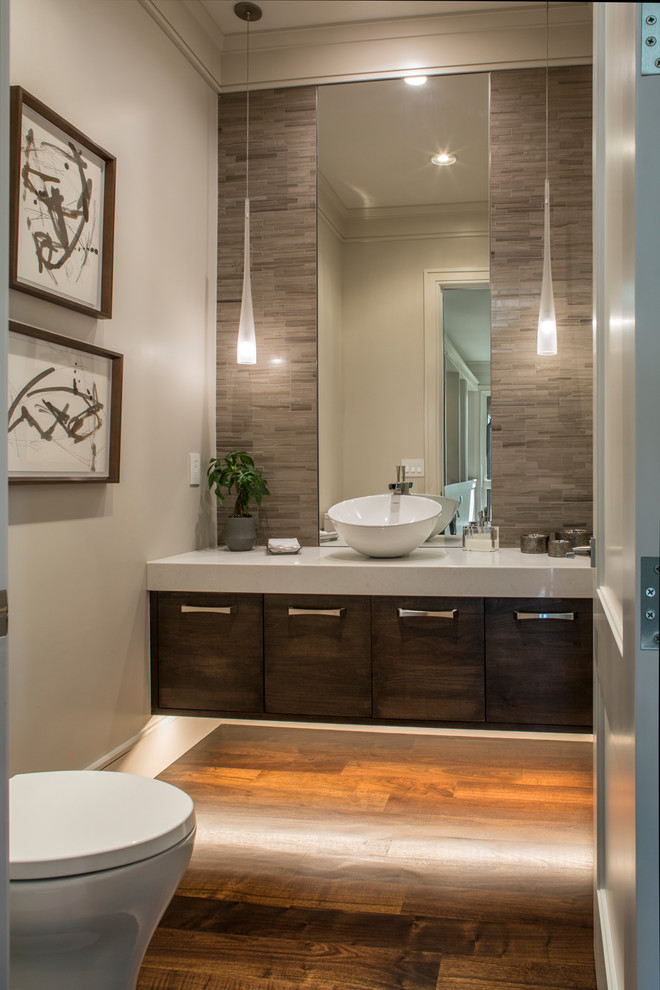 Inspiration for a mid-sized transitional powder room in Other with flat-panel cabinets, dark wood cabinets, a one-piece toilet, gray tile, stone tile, white walls, dark hardwood floors, a vessel sink, engineered quartz benchtops and brown floor.