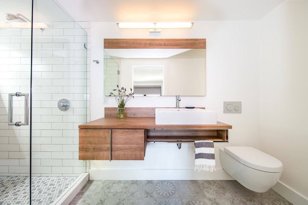 Inspiration for a contemporary 3/4 bathroom in San Francisco with flat-panel cabinets, light wood cabinets, an alcove shower, a wall-mount toilet, subway tile, white walls, a console sink, wood benchtops, grey floor and a hinged shower door.