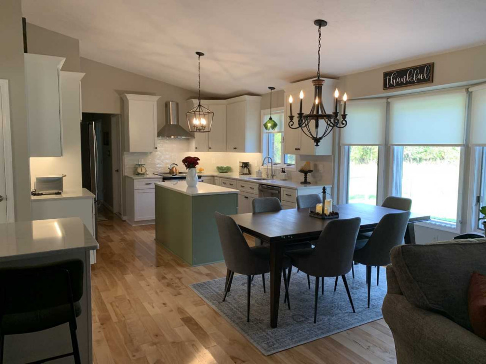 Example of a mid-sized transitional l-shaped light wood floor eat-in kitchen design in Baltimore with an undermount sink, shaker cabinets, green cabinets, quartz countertops, white backsplash, subway tile backsplash, stainless steel appliances, an island and multicolored countertops