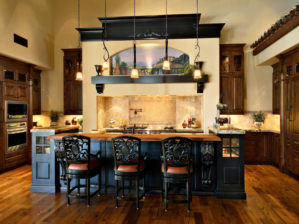 Large mountain style u-shaped medium tone wood floor open concept kitchen photo in Phoenix with raised-panel cabinets, brown cabinets, granite countertops, beige backsplash, stone tile backsplash, paneled appliances, an island and a farmhouse sink