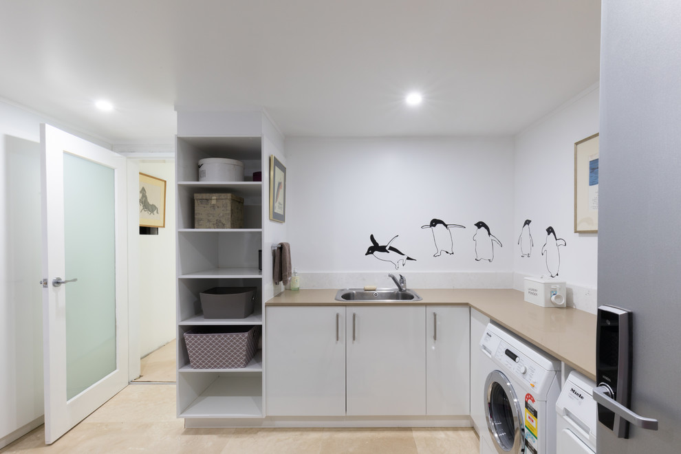 Photo of a large modern galley laundry room in Canberra - Queanbeyan with a double-bowl sink, flat-panel cabinets, granite benchtops, ceramic floors, beige floor and white cabinets.