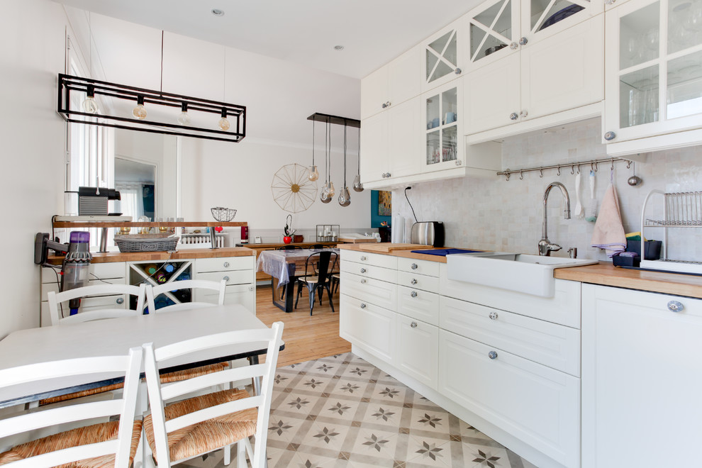Inspiration for a large country l-shaped open plan kitchen in Bordeaux with a farmhouse sink, glass-front cabinets, white cabinets, wood benchtops, beige splashback, limestone splashback, stainless steel appliances, cement tiles, with island, white floor and brown benchtop.