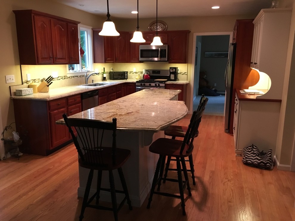 Transitional u-shaped light wood floor eat-in kitchen photo in Boston with an undermount sink, raised-panel cabinets, granite countertops, subway tile backsplash, stainless steel appliances and an island