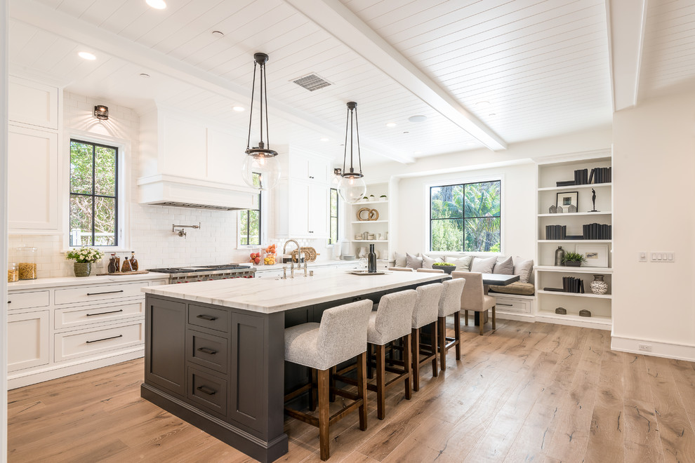 Photo of a transitional galley eat-in kitchen in Los Angeles with a farmhouse sink, shaker cabinets, white cabinets, stainless steel appliances and light hardwood floors.