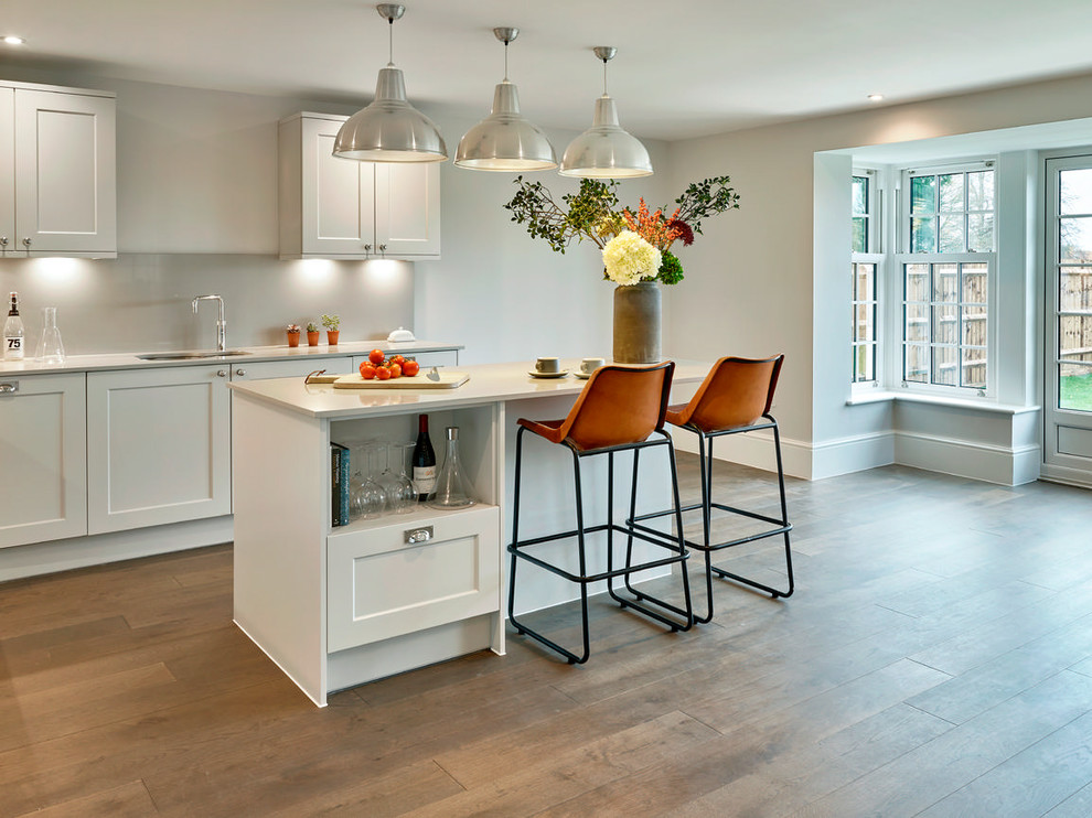 This is an example of a mid-sized transitional kitchen in London with an integrated sink, louvered cabinets, white splashback, white appliances, painted wood floors, a peninsula and brown floor.