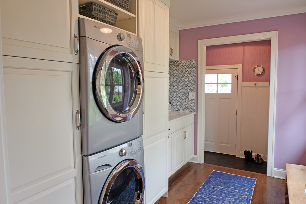 This is an example of a small transitional single-wall utility room in Chicago with white cabinets, purple walls, medium hardwood floors, a stacked washer and dryer, raised-panel cabinets, quartz benchtops and an undermount sink.