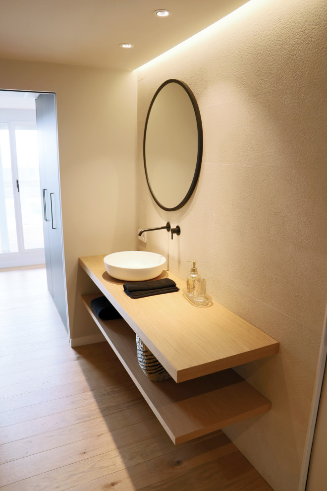 This is an example of a large modern master bathroom in Valencia with open cabinets, white cabinets, an alcove shower, a wall-mount toilet, beige tile, ceramic tile, beige walls, medium hardwood floors, a vessel sink, wood benchtops, a sliding shower screen, a single vanity and a built-in vanity.
