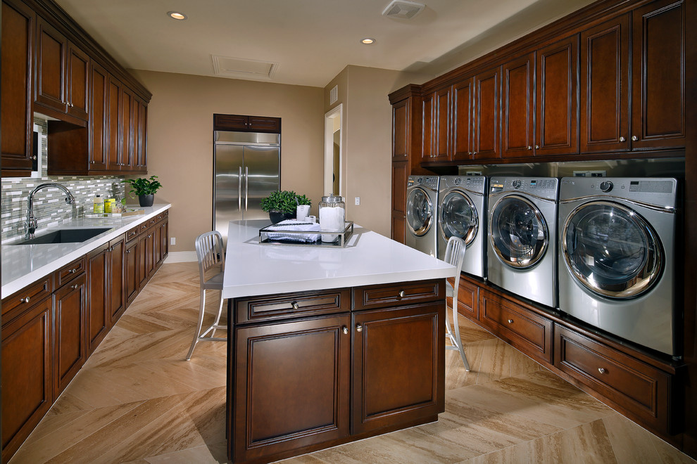 Galley dedicated laundry room in San Diego with a single-bowl sink, raised-panel cabinets, dark wood cabinets, quartz benchtops, beige walls, travertine floors and a side-by-side washer and dryer.