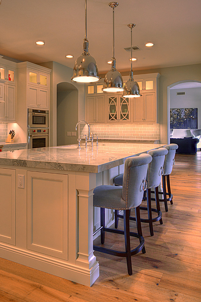 Kitchen - large transitional l-shaped medium tone wood floor kitchen idea in Phoenix with an undermount sink, recessed-panel cabinets, white cabinets, gray backsplash, subway tile backsplash, stainless steel appliances and an island