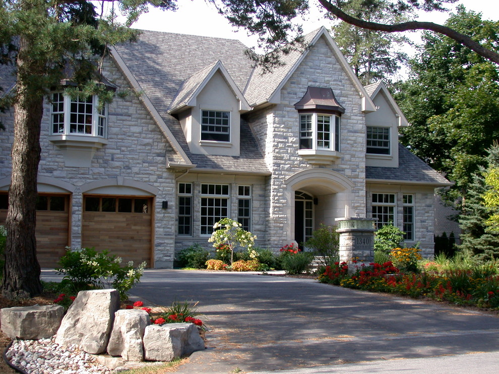 Large traditional two-storey grey house exterior in Toronto with mixed siding, a clipped gable roof and a shingle roof.
