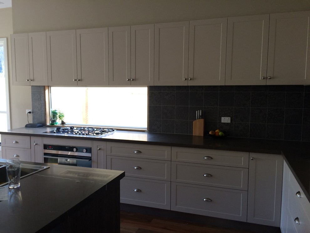 This is an example of a mid-sized traditional l-shaped eat-in kitchen in Melbourne with with island, a double-bowl sink, recessed-panel cabinets, beige cabinets, quartz benchtops, black splashback, ceramic splashback, stainless steel appliances and medium hardwood floors.