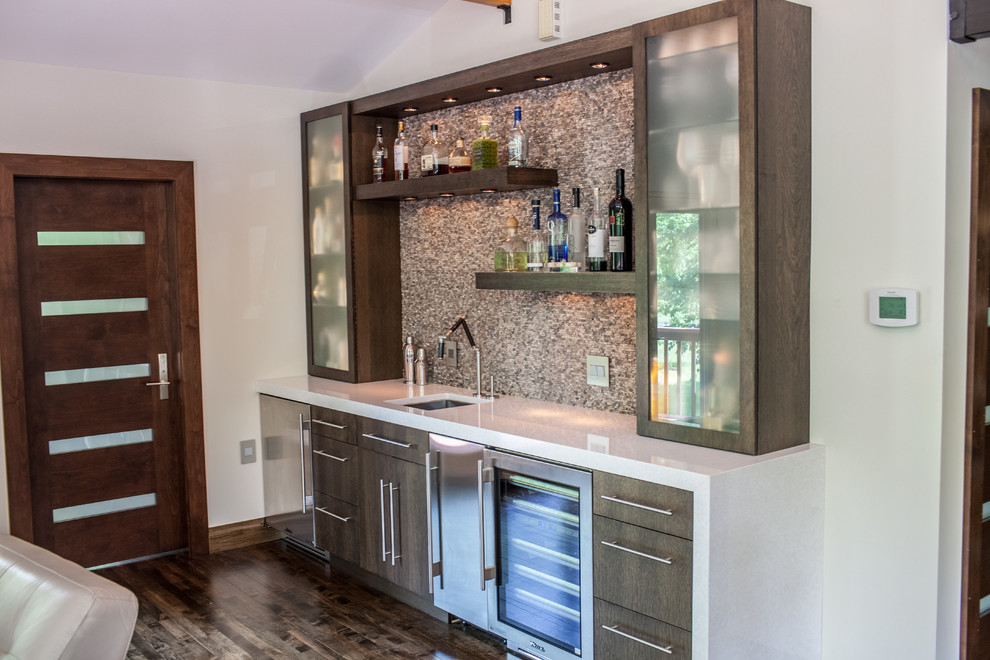 Small transitional single-wall wet bar in Philadelphia with an undermount sink, flat-panel cabinets, solid surface benchtops, grey splashback, mosaic tile splashback, dark hardwood floors and brown cabinets.