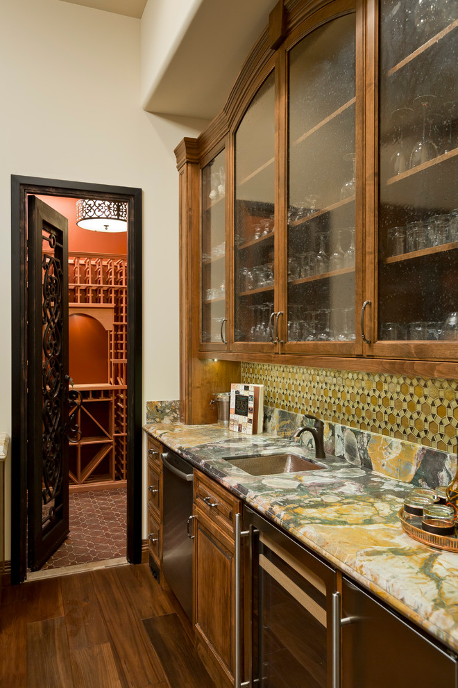 Mediterranean single-wall wet bar in Phoenix with an undermount sink, raised-panel cabinets, medium wood cabinets, multi-coloured splashback, mosaic tile splashback and dark hardwood floors.