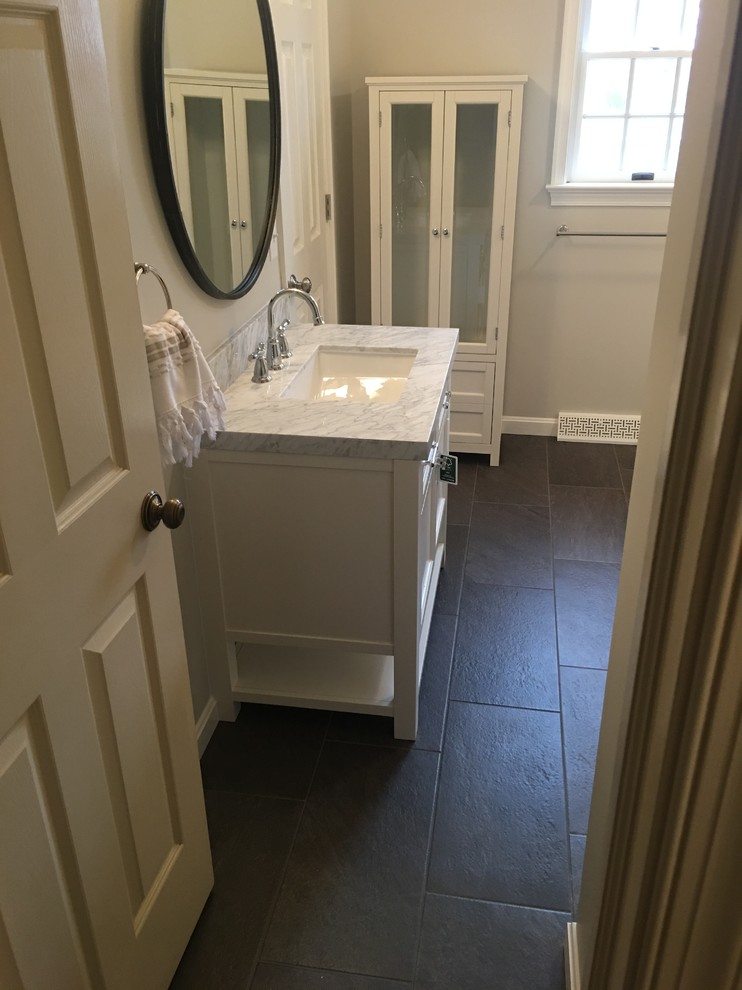 Example of a mid-sized classic 3/4 porcelain tile and gray tile porcelain tile and black floor alcove bathtub design with shaker cabinets, white cabinets, white walls, an undermount sink, marble countertops and a two-piece toilet