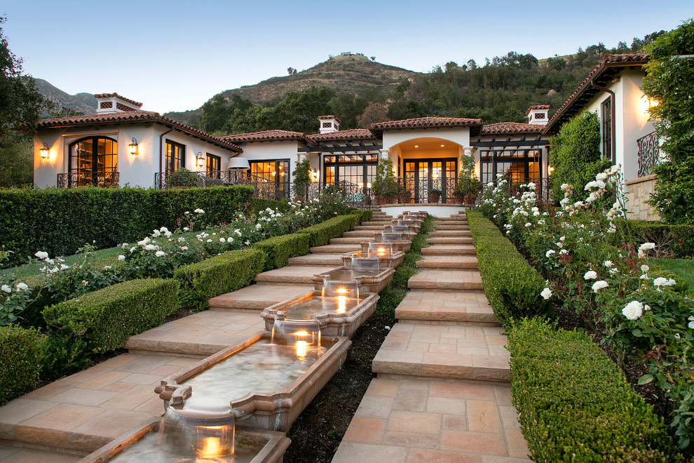 Mediterranean backyard formal garden in Santa Barbara with a water feature and natural stone pavers.