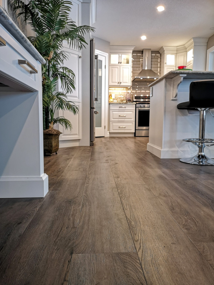 Example of a mid-sized transitional u-shaped light wood floor and brown floor enclosed kitchen design in Toronto with an undermount sink, raised-panel cabinets, white cabinets, granite countertops, beige backsplash, glass tile backsplash, stainless steel appliances, a peninsula and gray countertops
