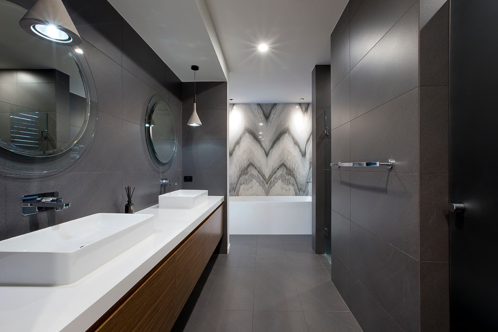 This is an example of a modern master bathroom in Gold Coast - Tweed with raised-panel cabinets, engineered quartz benchtops, gray tile, stone tile, a freestanding tub, an alcove shower, a wall-mount toilet, grey walls and a vessel sink.
