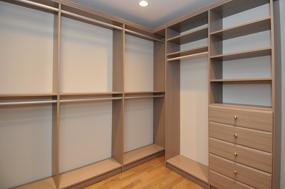 Photo of a traditional gender-neutral walk-in wardrobe in New York with flat-panel cabinets, brown cabinets, light hardwood floors and orange floor.