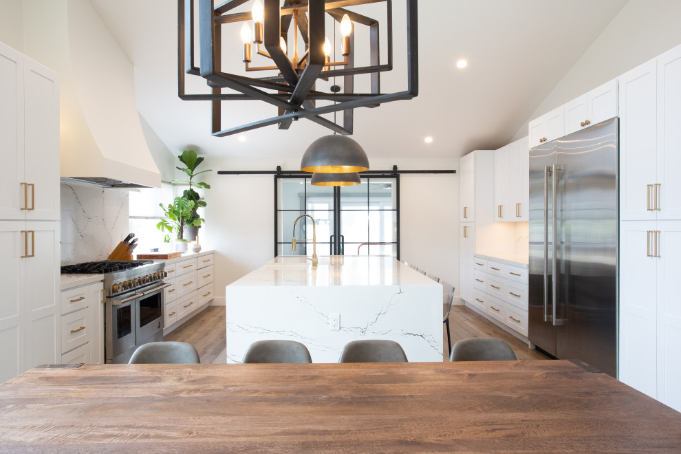 Inspiration for a mid-sized transitional galley brown floor eat-in kitchen remodel in Orange County with a farmhouse sink, shaker cabinets, white cabinets, white backsplash, stainless steel appliances, an island and white countertops