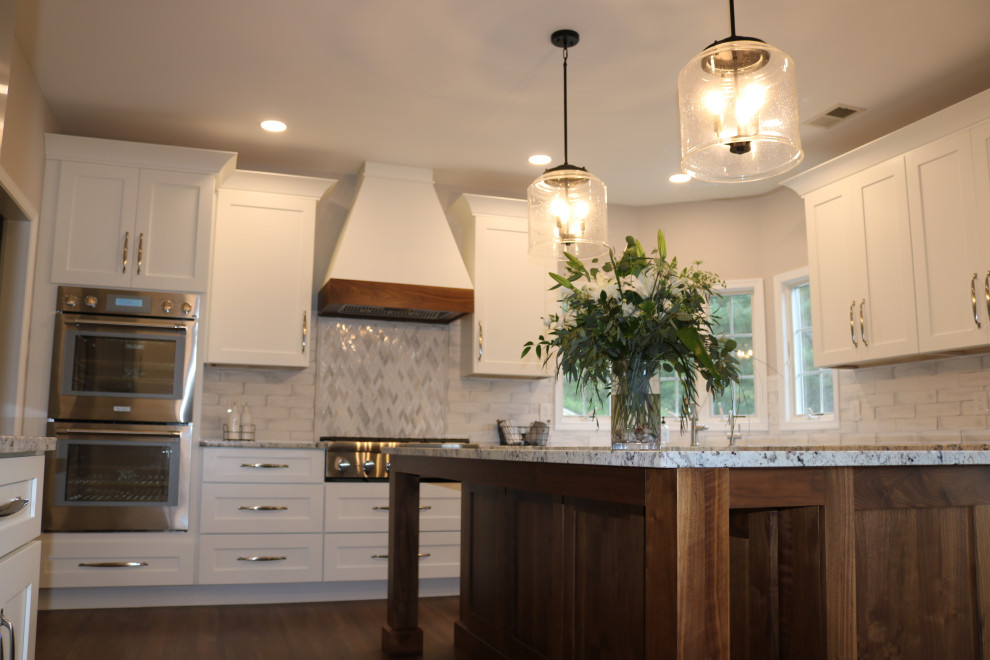 Bild på ett stort vintage vit vitt kök och matrum, med en rustik diskho, skåp i shakerstil, granitbänkskiva, vitt stänkskydd, stänkskydd i tunnelbanekakel, rostfria vitvaror, mellanmörkt trägolv och en köksö