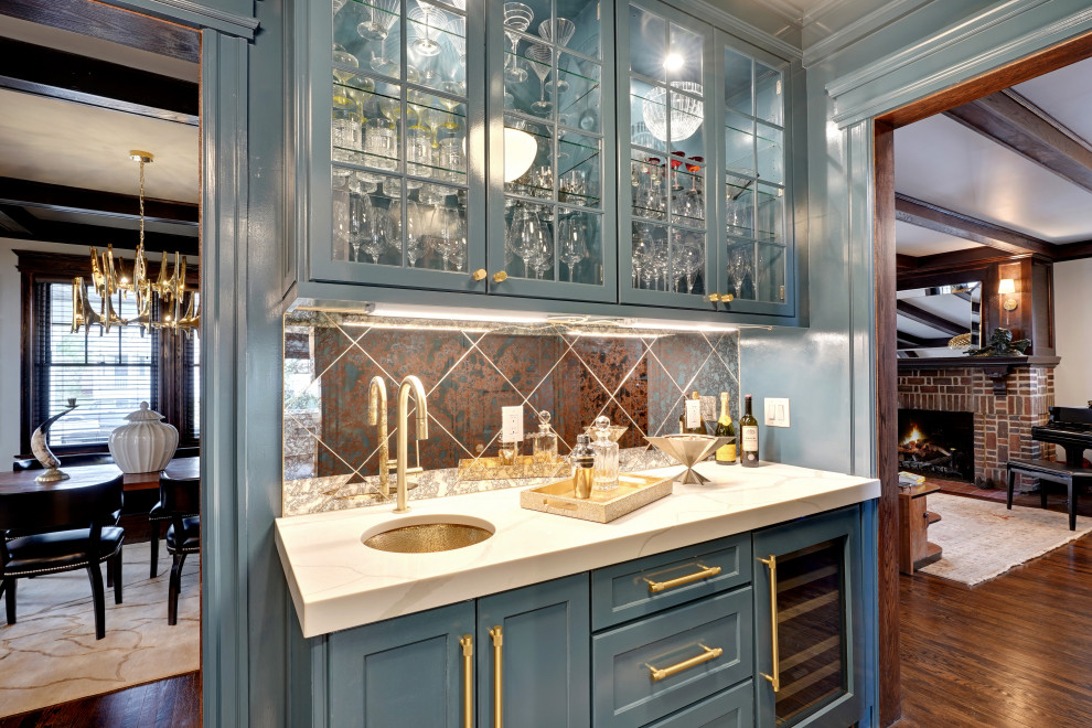 This is an example of a small transitional single-wall wet bar in New York with an undermount sink, glass-front cabinets, blue cabinets, quartz benchtops, glass tile splashback, medium hardwood floors, brown floor and white benchtop.