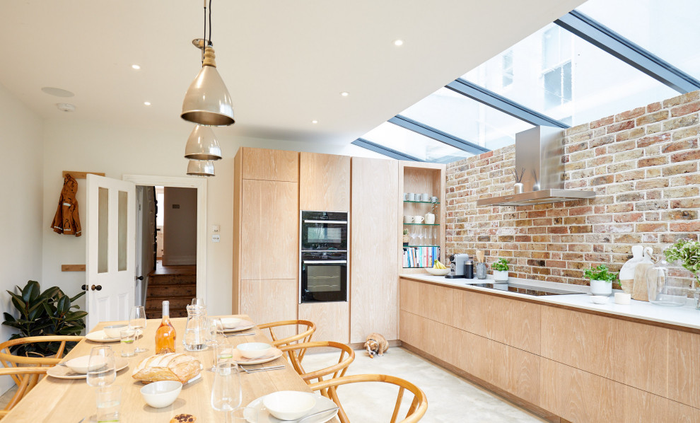 Inspiration for a mid-sized contemporary l-shaped eat-in kitchen in Sussex with flat-panel cabinets, light wood cabinets, brown splashback, brick splashback, black appliances, no island, grey floor and white benchtop.