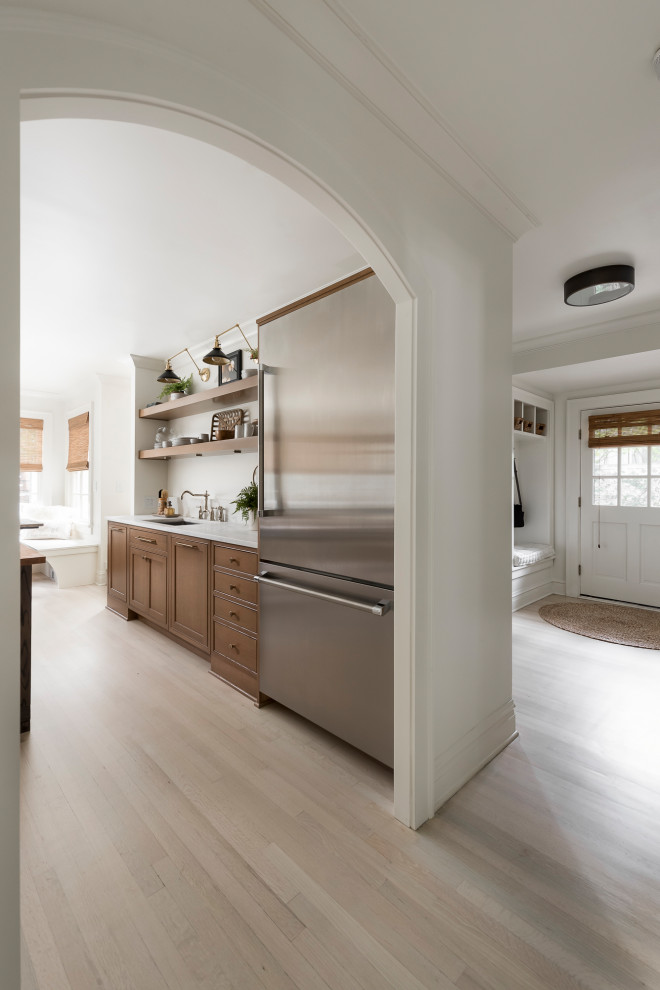Inspiration for a mid-sized traditional galley separate kitchen in Chicago with a drop-in sink, beaded inset cabinets, medium wood cabinets, marble benchtops, metallic splashback, mirror splashback, stainless steel appliances, light hardwood floors, with island, brown floor and white benchtop.