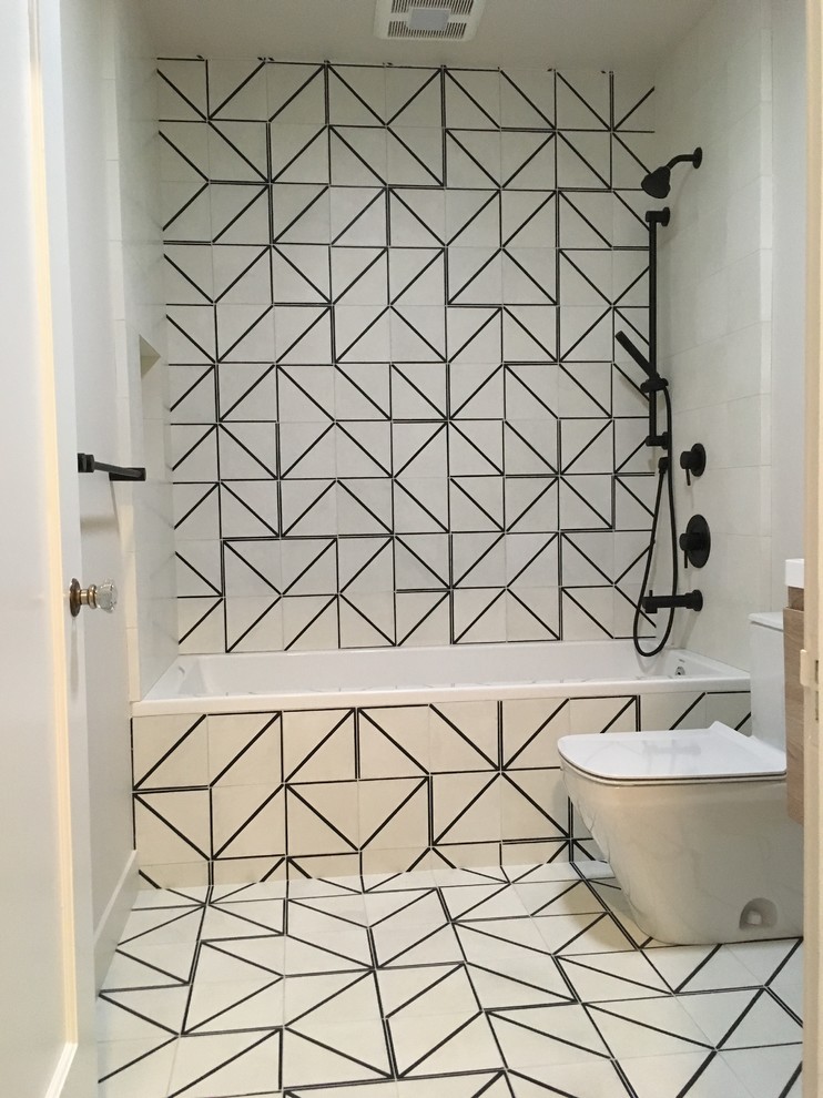 Photo of a small modern bathroom in San Francisco with flat-panel cabinets, light wood cabinets, a drop-in tub, a shower/bathtub combo, a one-piece toilet, black and white tile, cement tile, white walls, cement tiles, a wall-mount sink, solid surface benchtops, a hinged shower door and white benchtops.