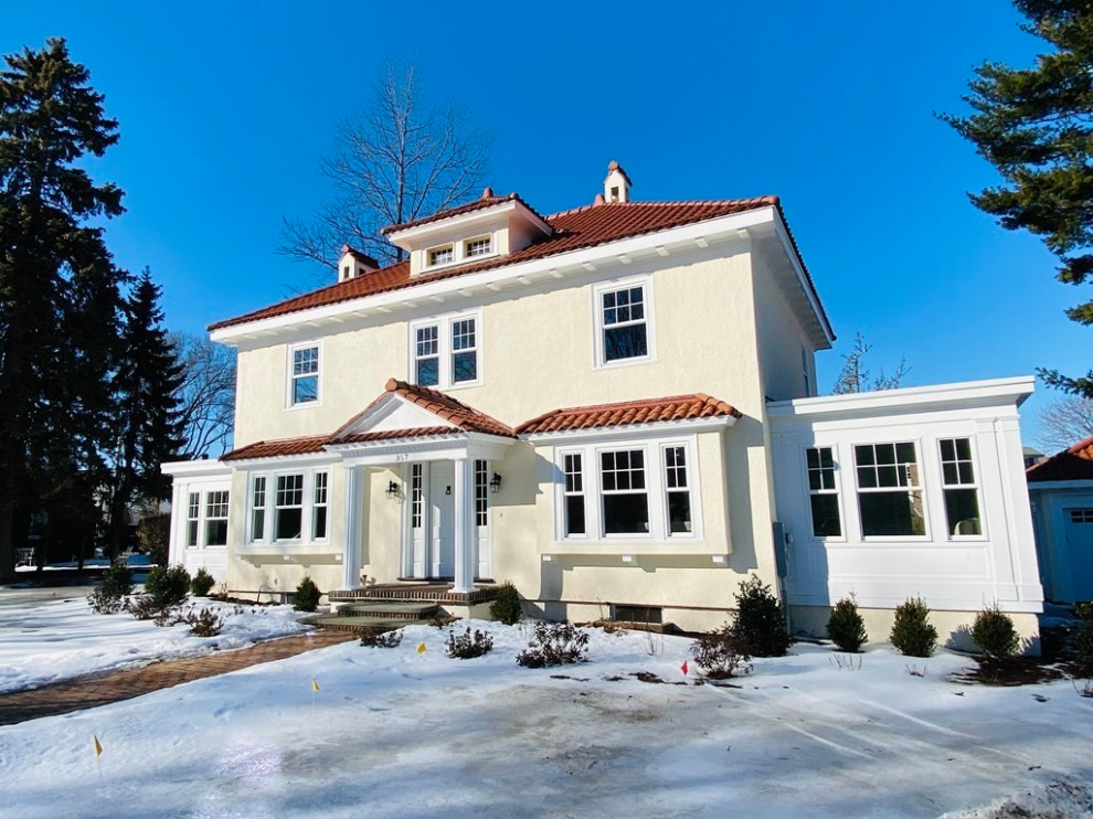 Cette image montre une façade de maison beige traditionnelle à deux étages et plus avec un toit à quatre pans, un toit en tuile et un toit rouge.