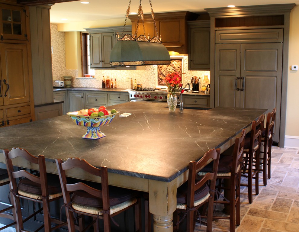 Mid-sized traditional l-shaped eat-in kitchen in Philadelphia with a farmhouse sink, beaded inset cabinets, distressed cabinets, soapstone benchtops, with island and stainless steel appliances.
