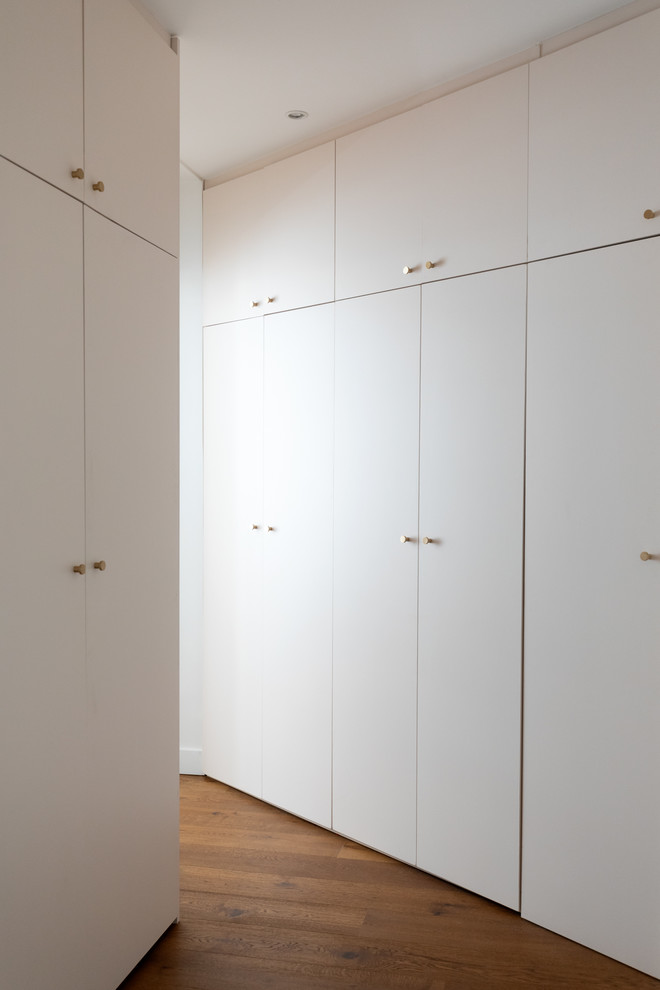 This is an example of a small contemporary gender-neutral walk-in wardrobe in Paris with beaded inset cabinets, beige cabinets, dark hardwood floors and brown floor.