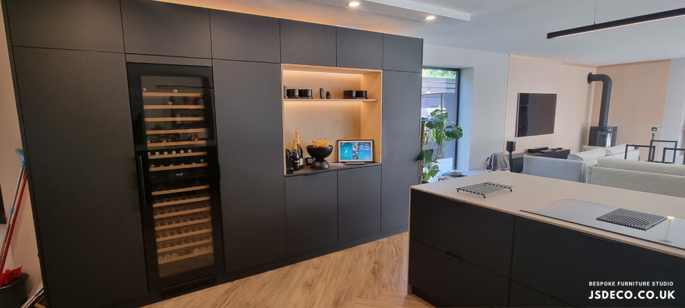Large contemporary open plan kitchen in Manchester with a drop-in sink, flat-panel cabinets, black cabinets, laminate benchtops, black appliances, light hardwood floors, with island, beige floor and beige benchtop.