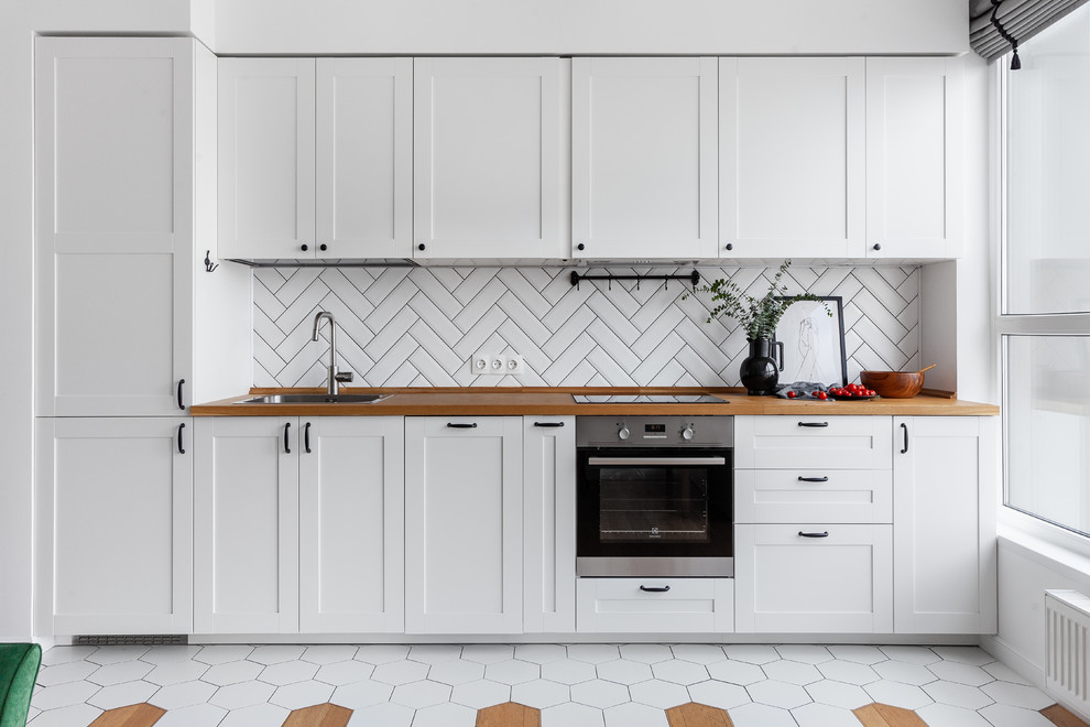 Inspiration for a scandinavian single-wall kitchen in Moscow with shaker cabinets, white cabinets, white splashback, stainless steel appliances, no island, a single-bowl sink, wood benchtops and multi-coloured floor.