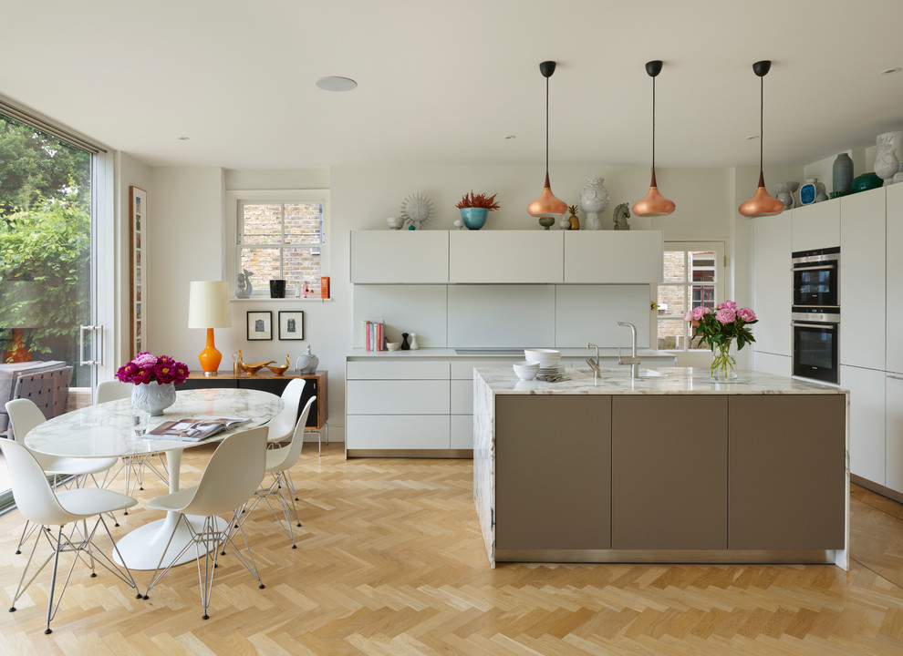 Design ideas for a mid-sized contemporary l-shaped eat-in kitchen in Other with an undermount sink, flat-panel cabinets, white cabinets, marble benchtops, white splashback, white appliances, light hardwood floors, with island and beige floor.