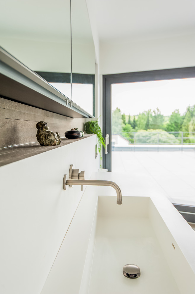 Badezimmer With integriertem Waschbecken, flächenbündigen Schrankfronten, Mineralwerkstoff-Waschtisch, freistehender Badewanne, offener Dusche, Wandtoilette, braunen Fliesen, Steinfliesen and weißer Wandfarbe in Frankfurt