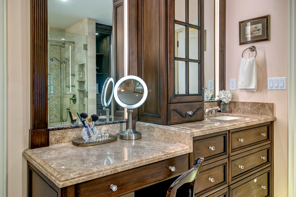 This is an example of a mid-sized traditional master bathroom in San Diego with furniture-like cabinets, medium wood cabinets, an undermount tub, a corner shower, beige tile, stone tile, pink walls, marble floors, marble benchtops and an undermount sink.